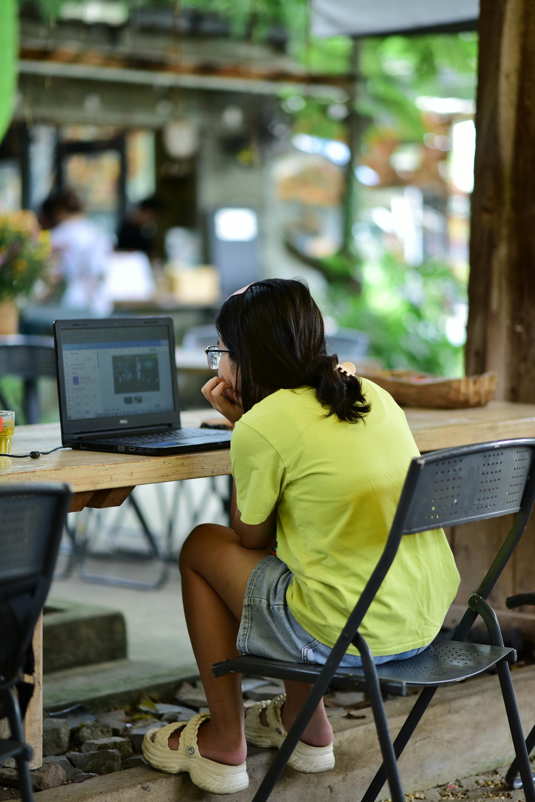 Teenager focused on a laptop at an outdoor café, embodying modern digital lifestyle.